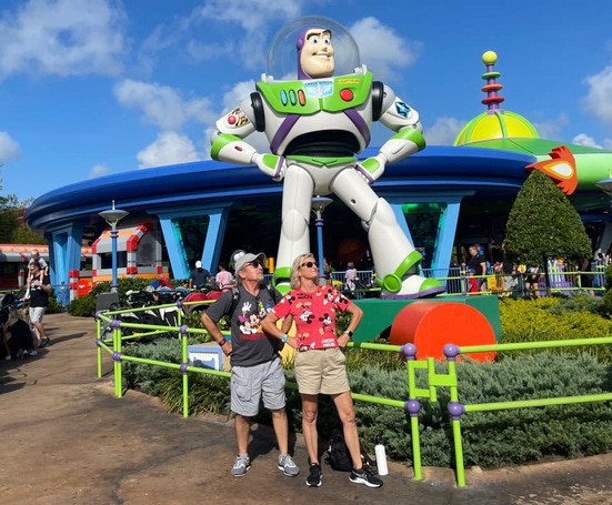 Couple posing with in Buzz Lightyear stance in front of Buzz Lightyear statue.