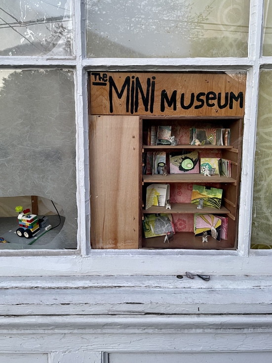 A mini museum nestled into the open space behind a missing pane of a glass window. 
