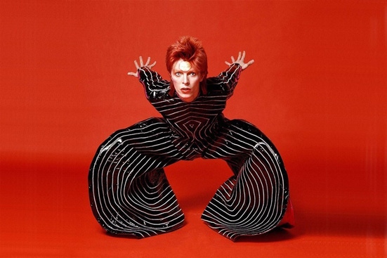 A studio photograph of David Bowie on a red background.