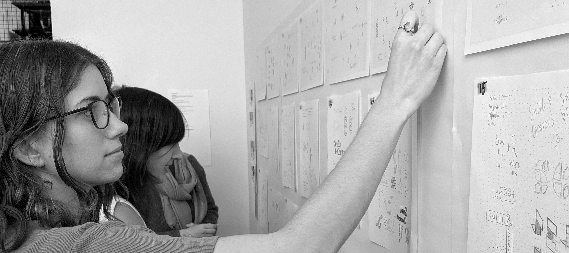 Women looking at handwritten papers hanging on wall.