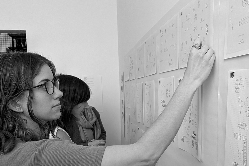 Women looking at handwritten papers hanging on wall. 