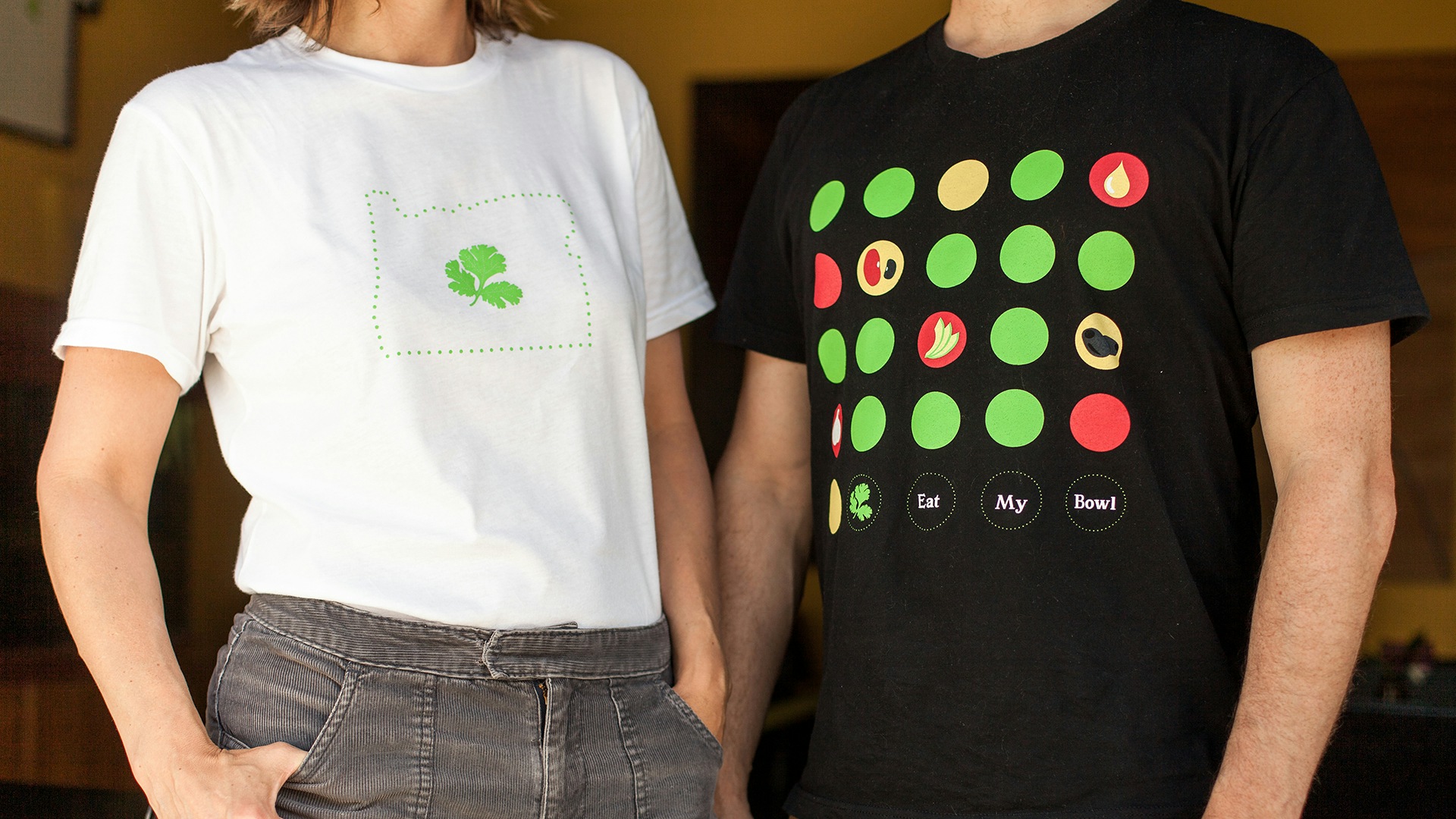 Two of the shirts we designed for Whole Bowl. The first is a white shirt with the Oregon state silhouette with the Whole Bowl cilantro leaf in the center. The second shirt features the illustrated menu items with the words "Eat my bowl" at the bottom.