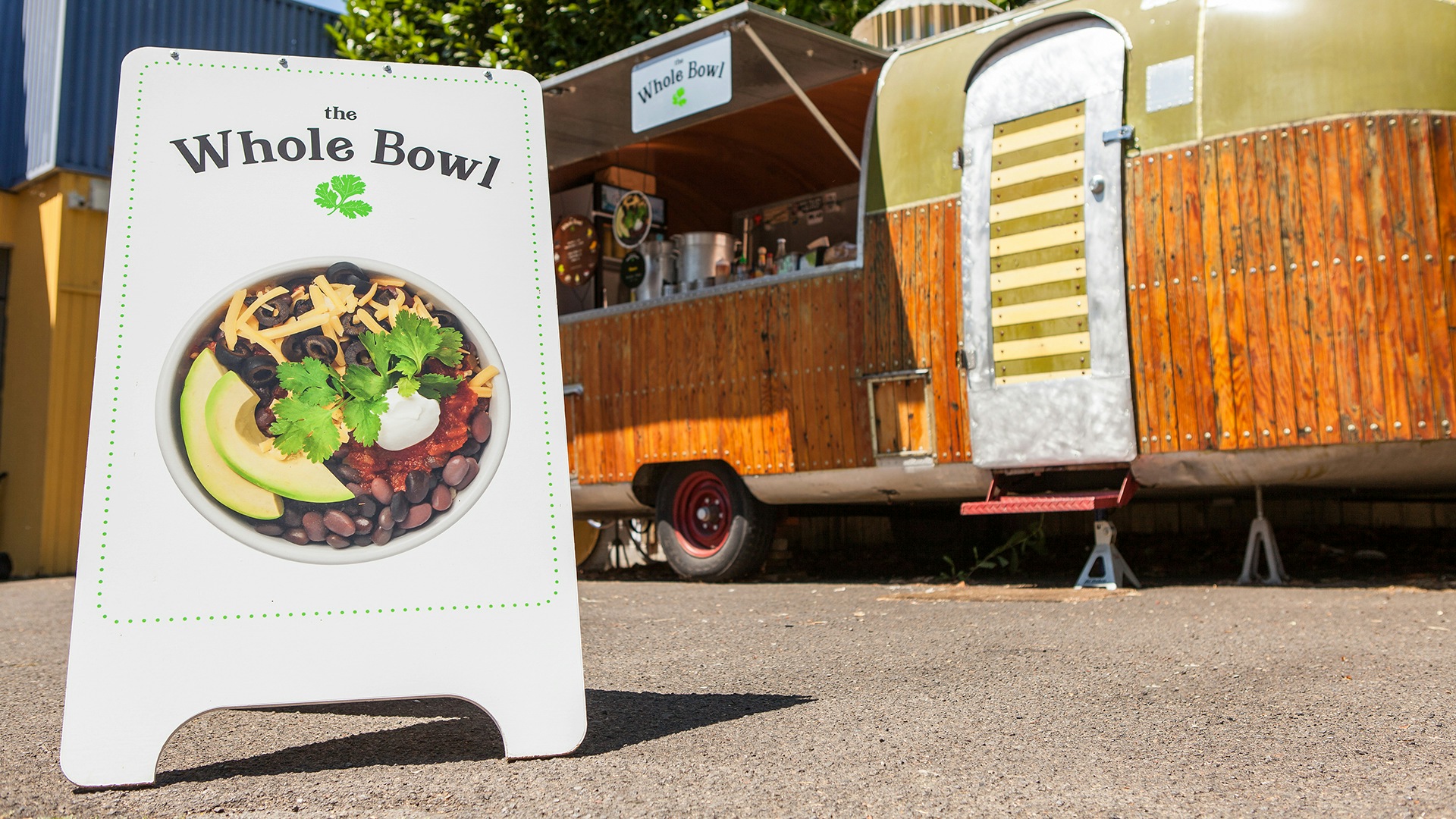 An a-frame sign featuring a photograph of the famous bowl sitting outside of a Whole Bowl food cart.