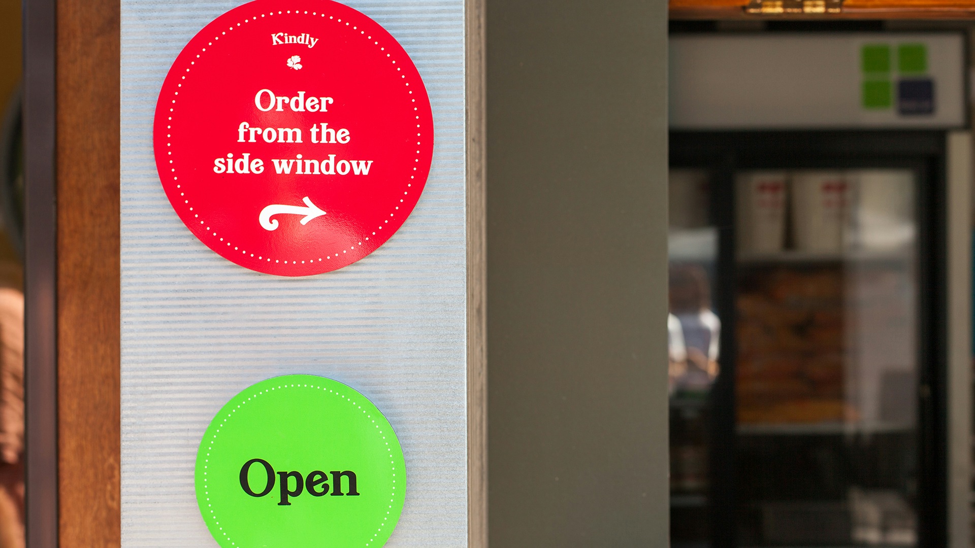 A photograph of restaurant's signgage. A green open sign set in the brand font, and another round sign in red that reads "Order from the side window."