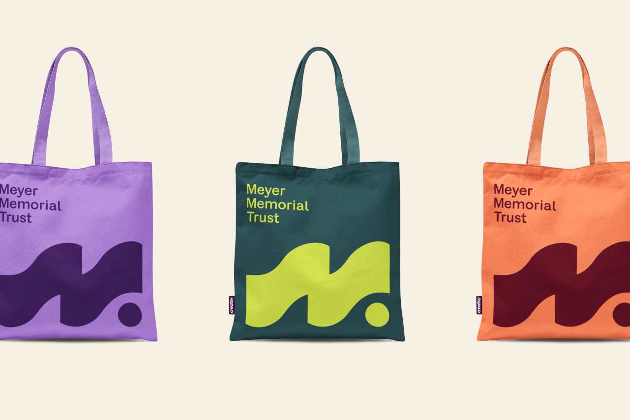 Three colorful Meyer Memorial Trust tote bags in purple, green, and orange, each with a bold wave-and-dot logo